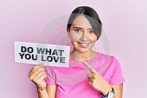 Beautiful young woman with short hair holding paper with do what you love text smiling happy pointing with hand and finger