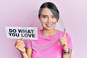 Beautiful young woman with short hair holding paper with do what you love text smiling with an idea or question pointing finger