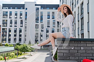 Beautiful young woman in shorts and a hat posing while sitting on a stone bench. A full-length portrait of a Caucasian