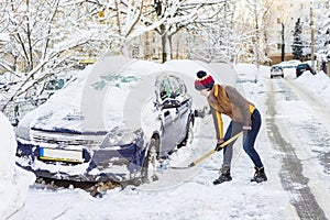 Beautiful young woman shoveling her car