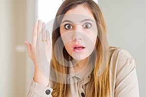 Beautiful young woman showing alliance ring on hand scared in shock with a surprise face, afraid and excited with fear expression