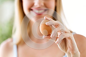 Beautiful young woman showing brown chiken egg at home.
