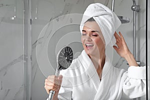 Beautiful young woman singing into showerhead in bathroom