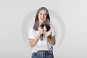 Beautiful young woman singing song in microphone at karaoke, standing white background