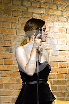 Beautiful young woman singing on vintage microphone on brick wall background