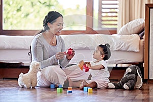 Beautiful young woman and single mother playing toy blocks with her adorable little baby daughter in the bedroom at home