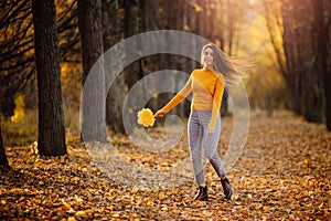 Beautiful young woman sits in autumn forest in yellow blouse with maple leaves and enjoys life. Freedom concept