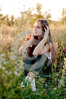 Beautiful young woman sits in grass and enjoys nature and sunset