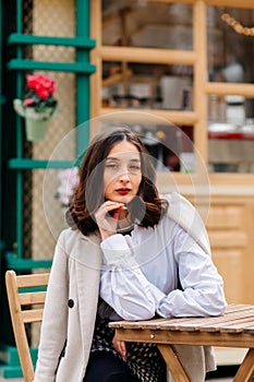 Beautiful young woman sits on a terrace near a cafe at a table