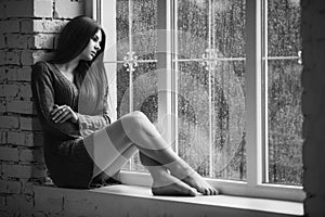 Beautiful young woman sitting alone close to window with rain drops. and sad girl. Concept of loneliness. Black