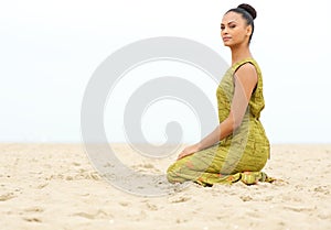 Beautiful young woman sitting alone on sand at the beach