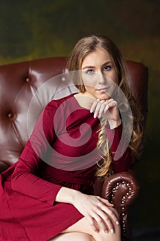 Beautiful young woman sitting in arm-chair. indoor. Looking in c