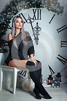 Beautiful young woman sitting on the background of a large clock Christmas decor, holding a flashlight, waiting for the holiday