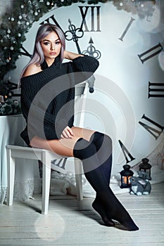 Beautiful young woman sitting on the background of a large clock Christmas decor, holding a flashlight, waiting for the holiday