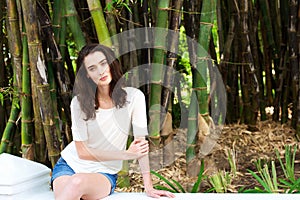 Beautiful young woman sitting by bamboo trees