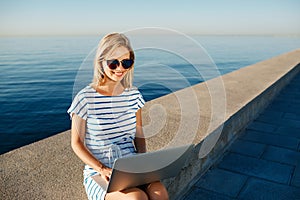 Beautiful young woman sitting on beach with laptop smiling and c