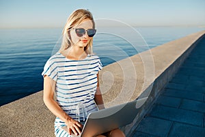 Beautiful young woman sitting on beach with laptop smiling and c