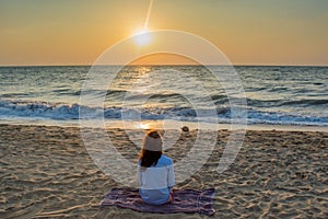 Beautiful young woman sitting on the beach near ocean during sunset