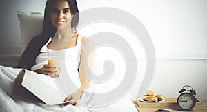 Beautiful young woman sitting in bed and having breakfast