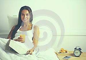 Beautiful young woman sitting in bed and having breakfast