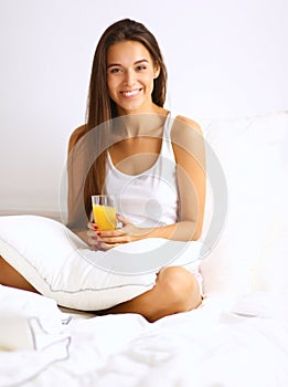 Beautiful young woman sitting in bed and having breakfast