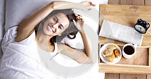 Beautiful young woman sitting in bed and having breakfast