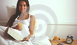 Beautiful young woman sitting in bed and having breakfast