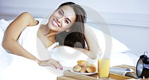 Beautiful young woman sitting in bed and having breakfast