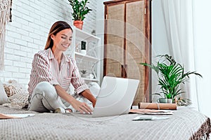 Beautiful young woman sitting on bed, working