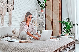 Beautiful young woman sitting on bed, working