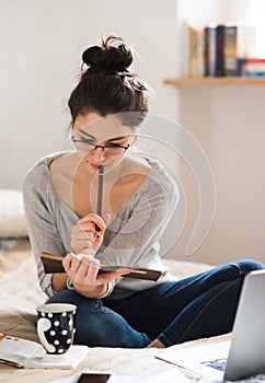 Beautiful young woman sitting on bed, working. Home office.