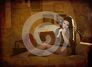 Beautiful young woman sitting on bed working on laptop having a red gramophone near her, in boudoir scenery. Attractive brunette