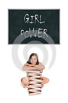 Beautiful young woman sitting behind a huge pile of books in front of a blackboard