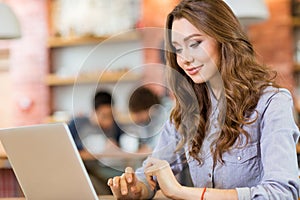 Beautiful young woman sitting in cafe and using laptop