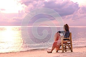 Beautiful young woman sitting in chair on the beach at sunset