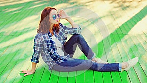 Beautiful young woman sitting the city park wearing sunglasses, shirt