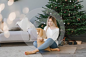 Beautiful young woman is sitting on a cozy sofa with pillows in a room decorated for the new year or Christmas