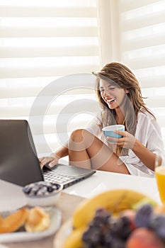 Woman using laptop computer while having breakfast