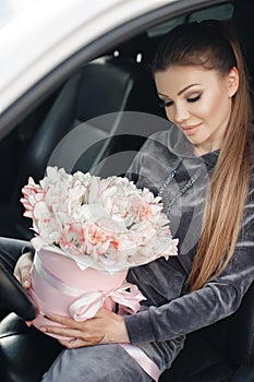 Beautiful young woman, sitting on the driver`s seat in a car with a pink box full of tender, white, with a pink edging of tult-col