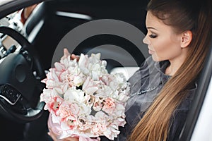 Beautiful young woman, sitting on the driver`s seat in a car with a pink box full of tender, white, with a pink edging of tult-col