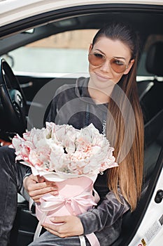 Beautiful young woman, sitting on the driver`s seat in a car with a pink box full of tender, white, with a pink edging of tult-col