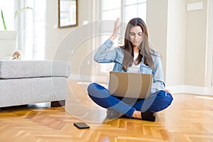 Beautiful young woman sitting on the floor with crossed legs using laptop annoyed and frustrated shouting with anger, crazy and