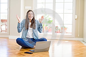 Beautiful young woman sitting on the floor with crossed legs using laptop celebrating mad and crazy for success with arms raised