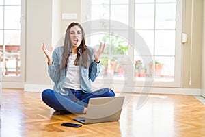 Beautiful young woman sitting on the floor with crossed legs using laptop crazy and mad shouting and yelling with aggressive