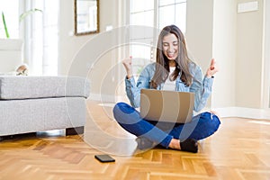 Beautiful young woman sitting on the floor with crossed legs using laptop screaming proud and celebrating victory and success very