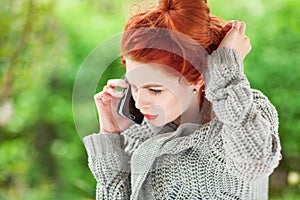 Beautiful young woman sitting in the garden having a conversation on her cell phone