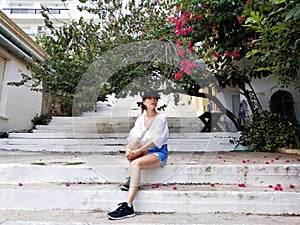 Beautiful young woman sitting on the old street of Agios Nikolaos, Crete, Greece. Bougainvillea blooming tree.