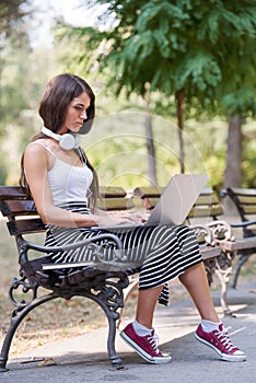 Beautiful young woman sitting in public park working on laptop computer