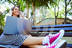 Beautiful young woman sitting in public park working on laptop computer