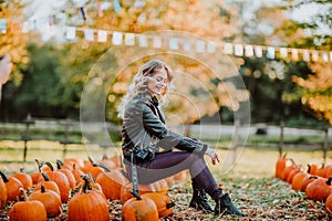 Beautiful young woman sitting on a pumpkin`s field. Autumn background